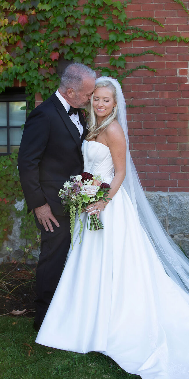 Groom kissing bride in front of historic brick wall