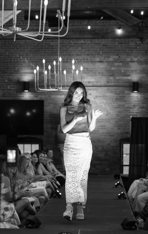 Woman walking down a catwalk waving in black and white